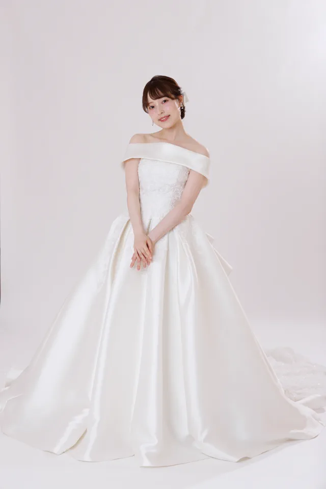 白い背景で、肩を出したサテンのウェディングドレスのモデル