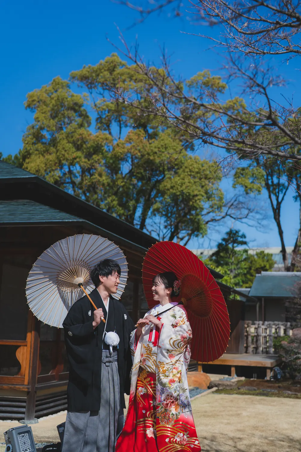 茶室の庭で、番傘を持つ色打掛の花嫁と新郎