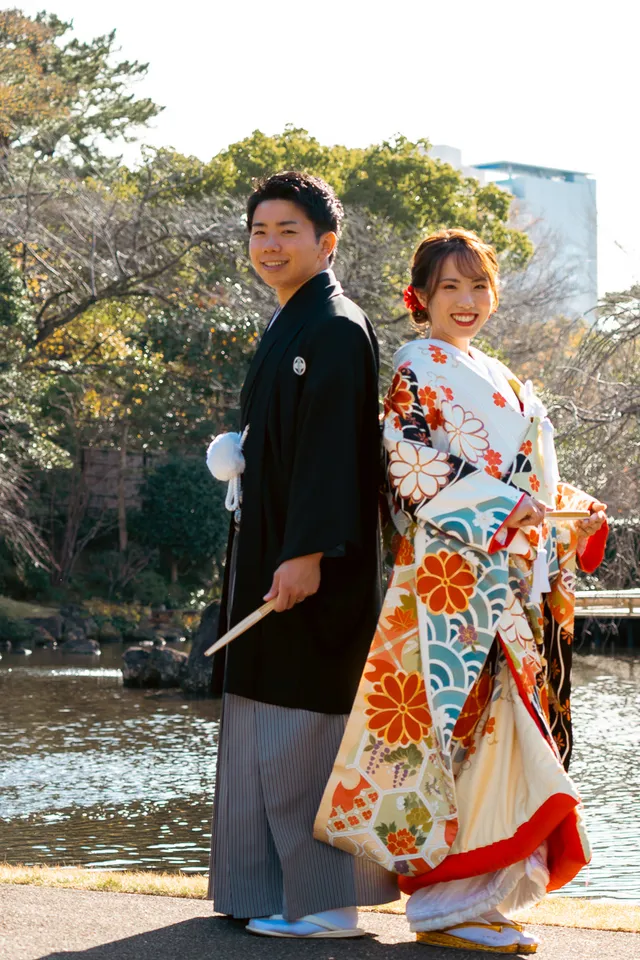 庭園の池のほとりに背中合わせで立つ、色打掛の花嫁と新郎