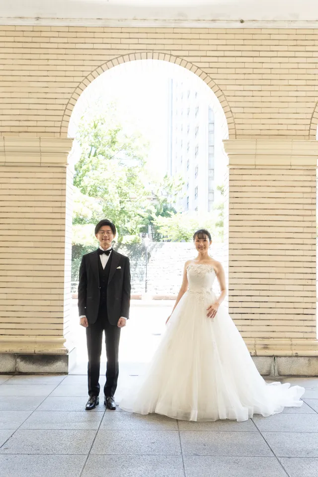 洋館の回廊のアーチの下に立つ、ウェディングドレスの花嫁と新郎