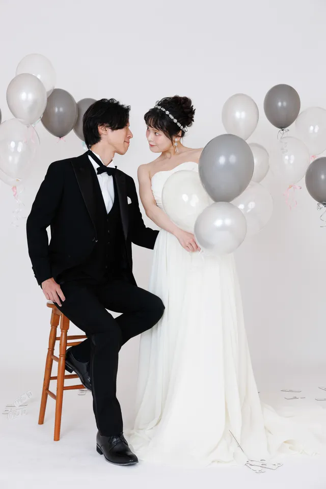白いスタジオで、風船に囲まれたウェディングドレスの花嫁と新郎