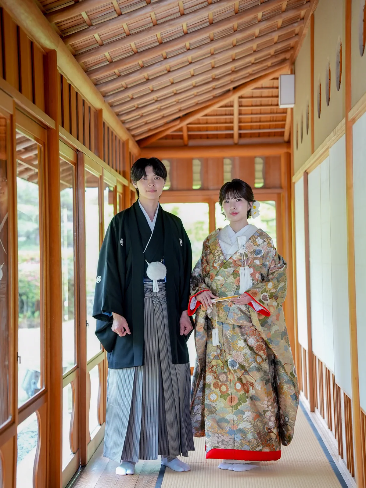 茶室の廊下に立つ、金と緑の色打掛の花嫁と黒紋付の新郎
