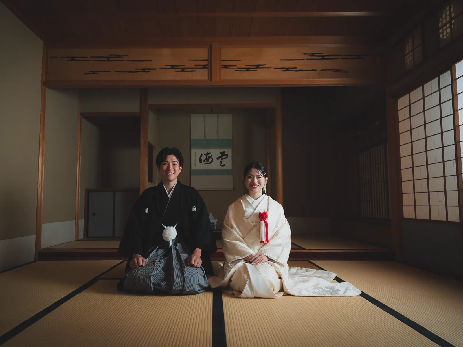 掛け軸のある和室で正座する、白無垢の花嫁と黒紋付の新郎