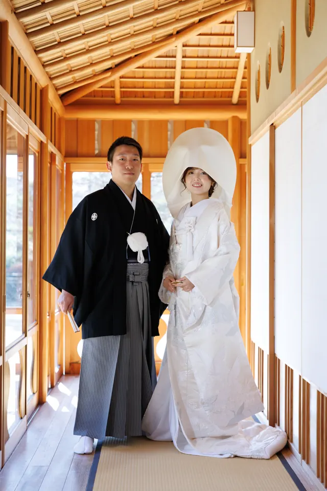 茶室の渡り廊下に立つ、綿帽子の白無垢の花嫁と新郎