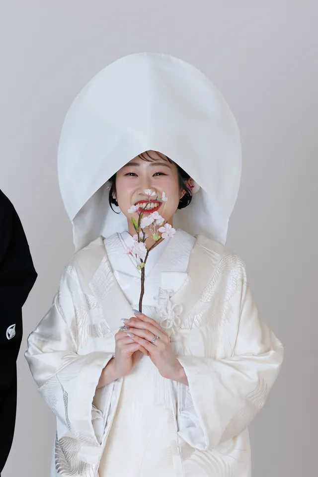 スタジオで、花の枝を持つ綿帽子の白無垢の花嫁